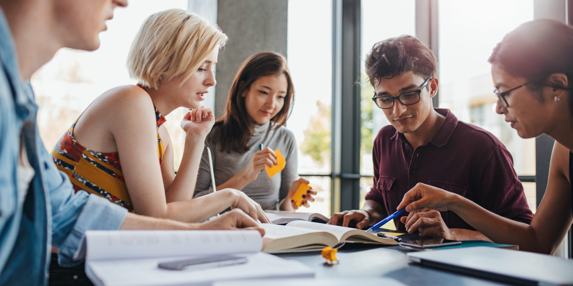 Diverse group of young people sitting at table reading books. University students in cooperation with their assignment at library.