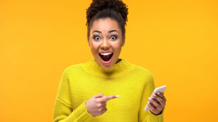 Joyful young woman pointing at smartphone in hand, online shopping application